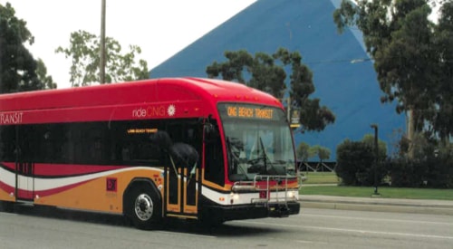 Red bus with orange and white swirls driving on the road in front of a triangular shaped building